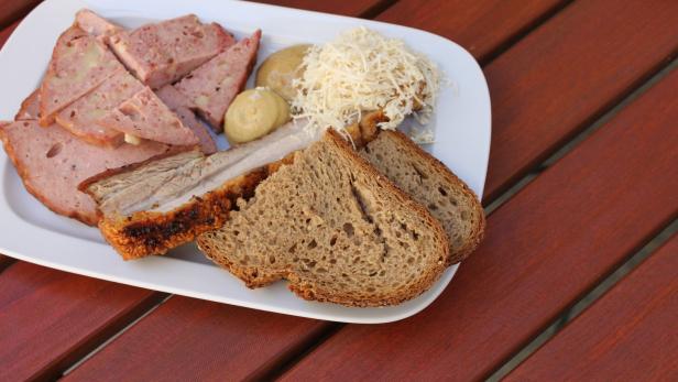 Eine Brotzeitplatte mit Leberkäse, Schweinebraten, Brot, Senf und Meerrettich auf einem Holztisch.