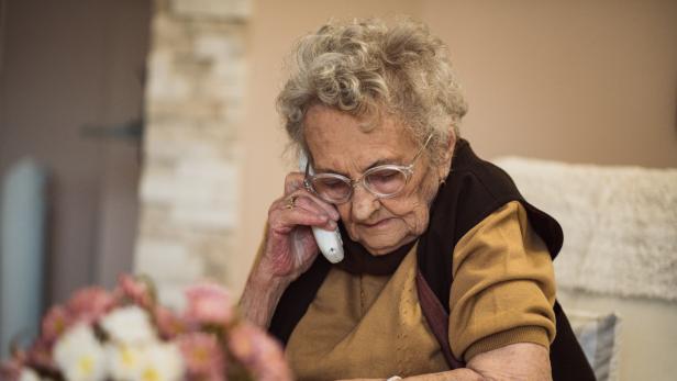 Eine ältere Frau mit Brille telefoniert mit einem weißen Telefon.