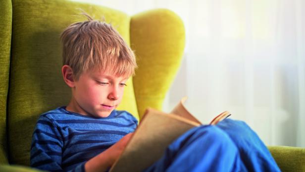 Little boy reading a book in green armchair