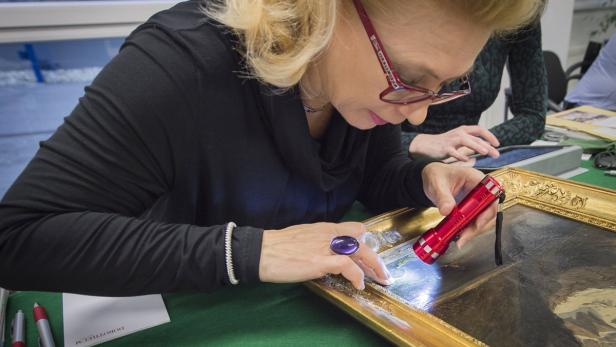 Eine Frau untersucht ein Gemälde mit einer kleinen, roten Taschenlampe.