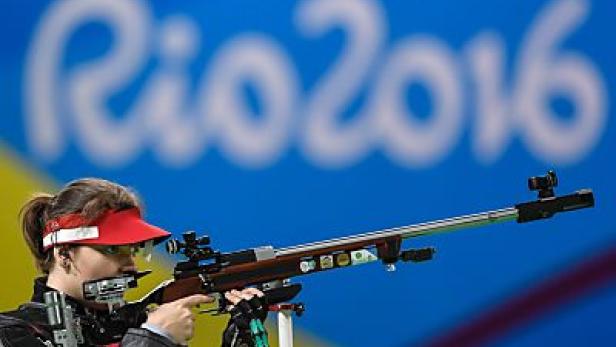 Eine Schützin zielt mit einem Gewehr vor dem Hintergrund des „Rio 2016“-Logos.