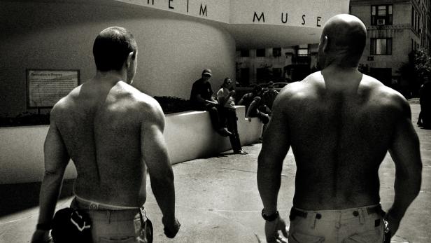Zwei Männer ohne Hemd stehen vor dem Guggenheim Museum in New York.