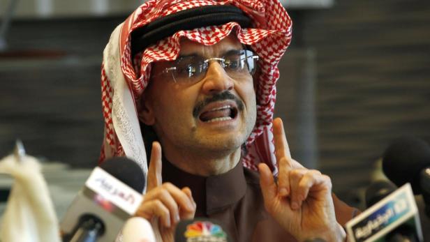 Ein Mann mit traditioneller Kopfbedeckung gestikuliert vor Mikrofonen.