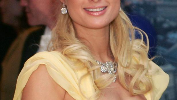 Paris Hilton in einem gelben Kleid mit Schmuck lächelt.