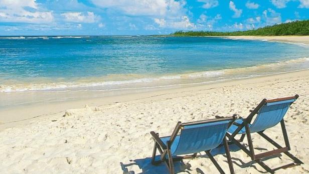 Zwei blaue Liegestühle stehen am Strand mit Blick auf das türkisfarbene Meer.