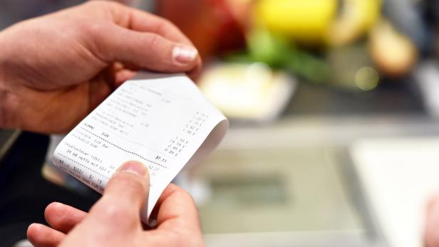 Hände halten einen Kassenbon mit einer Gesamtsumme von 37,11 Euro vor einem unscharfen Hintergrund.