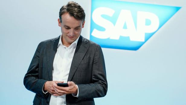 Ein Mann im Anzug blickt auf sein Smartphone vor einem SAP-Logo.