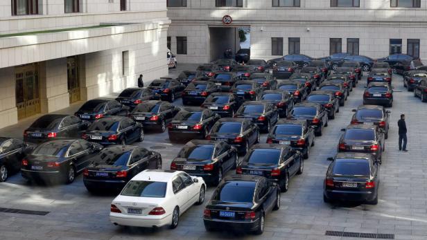 Viele schwarze Audis stehen in Reih und Glied auf einem Platz vor einem Gebäude.