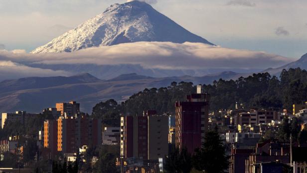 Blick auf eine Stadt vor einer Bergkette mit einem schneebedeckten Gipfel.