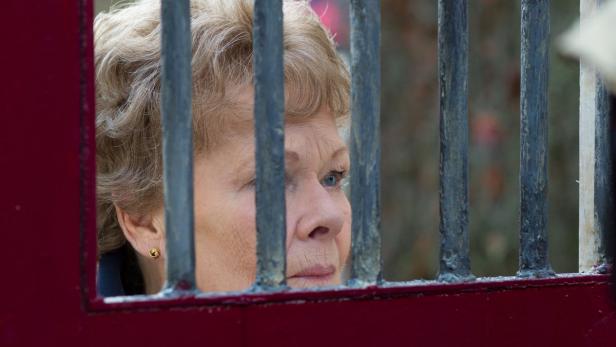 Eine ältere Frau blickt durch ein vergittertes Fenster.