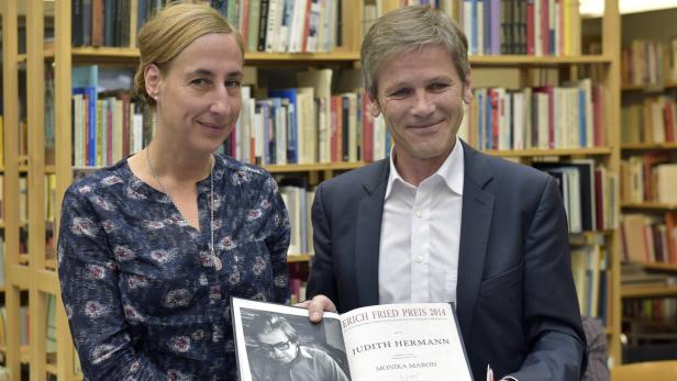 Judith Hermann und ein Mann präsentieren das Buch „Erich Fried Preis 2014“ vor einem Bücherregal.
