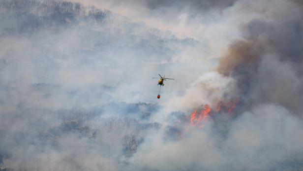 A helicopter carries river water as it flies over a wildfire in Sierra de Leyre