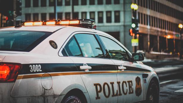 Ein Polizeiauto steht mit eingeschaltetem Blaulicht in einer städtischen Umgebung.