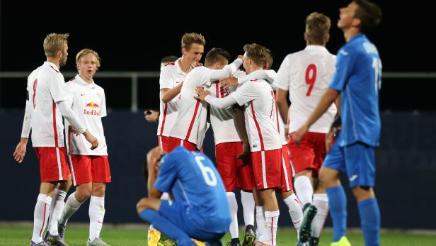 Fußballspieler in weißen und roten Trikots umarmen sich, während ein Spieler in Blau enttäuscht kniet.