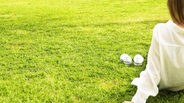 Eine Frau liegt im Gras, ihre weißen Turnschuhe stehen daneben.