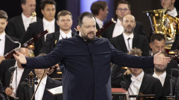 Ein Dirigent leitet ein Orchester mit Blasinstrumenten und Streichern.