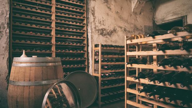Ein Weinkeller mit einem Fass und Regalen voller Weinflaschen.