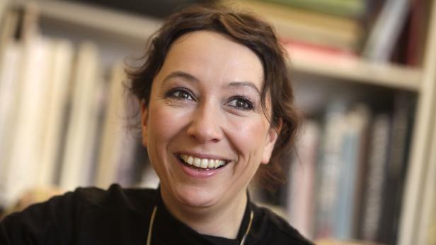 Eine lächelnde Frau mit braunen Haaren vor einem Bücherregal.