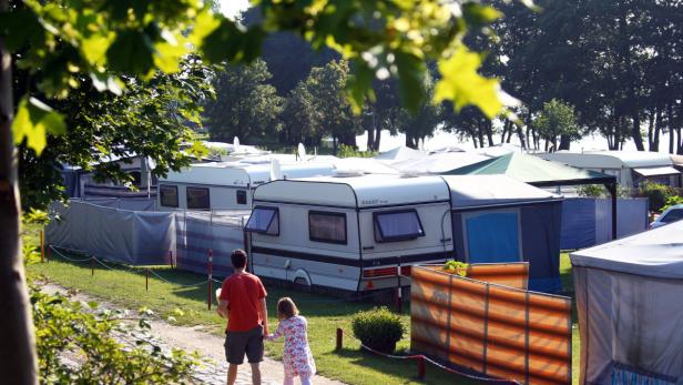 Ein Vater und seine Tochter spazieren über einen Campingplatz mit vielen Wohnwagen.
