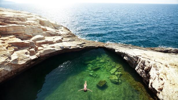 Eine Frau schwimmt in einem natürlichen Felsenpool am Meer.