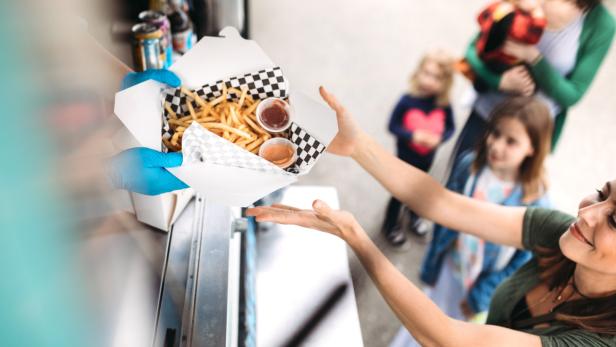 Eine Frau kauft an einem Imbisswagen eine Portion Pommes mit Dips für ihre Kinder.