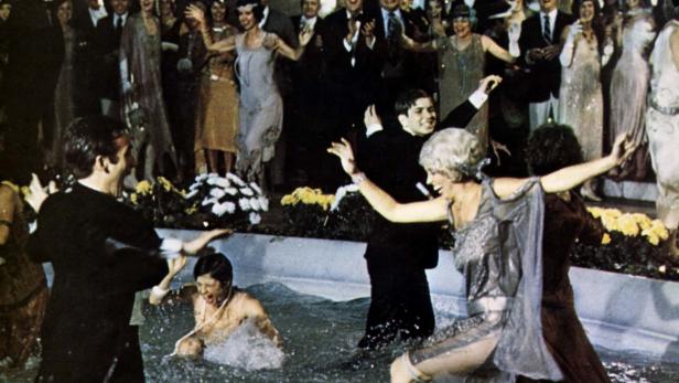 Gäste in Abendgarderobe springen in einen Pool auf einer Party.