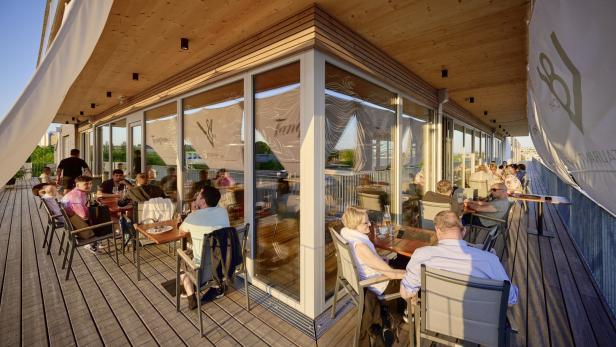 Gäste sitzen auf der Terrasse eines Restaurants mit Glasfront.