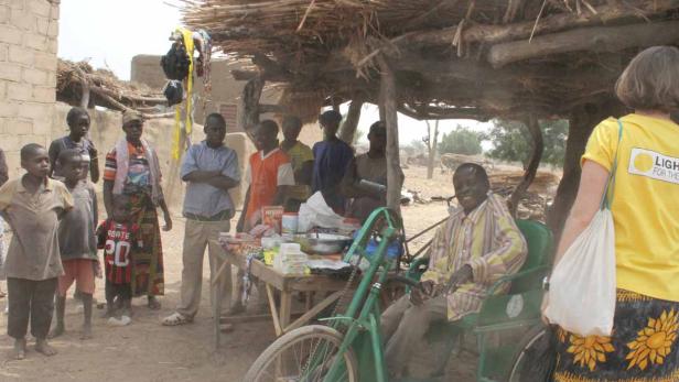 Eine Gruppe von Menschen steht vor einem kleinen Laden unter einem Strohdach.