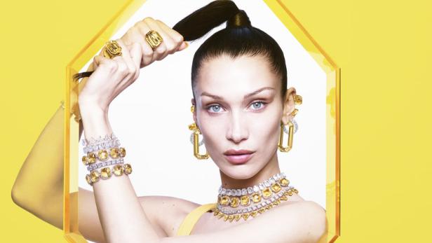 Bella Hadid präsentiert gelben Schmuck vor einem gelben Hintergrund.