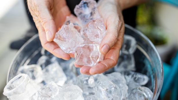 Eine Person hält eine Handvoll Eiswürfel über einen Eimer voller Eis.