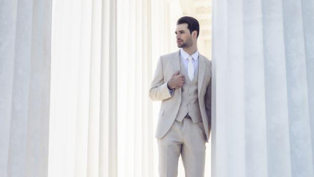 Ein Mann im Anzug steht zwischen weißen Säulen.