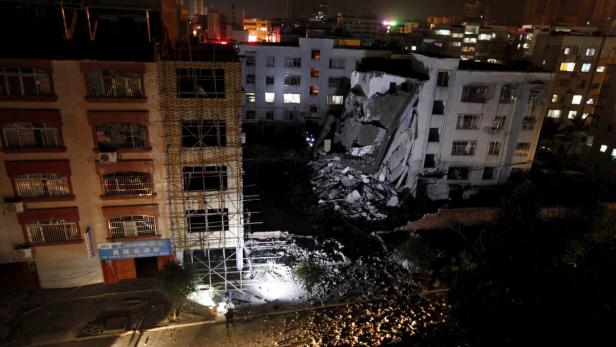 Ein teilweise eingestürztes Wohngebäude in einer Stadt bei Nacht.