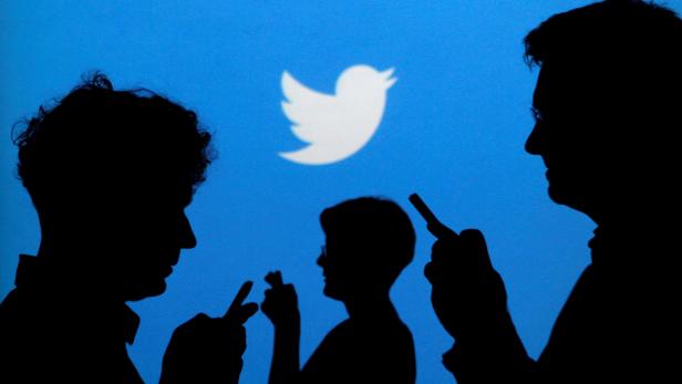 FILE PHOTO: People holding mobile phones are silhouetted against a backdrop projected with the Twitter logo  in Warsaw