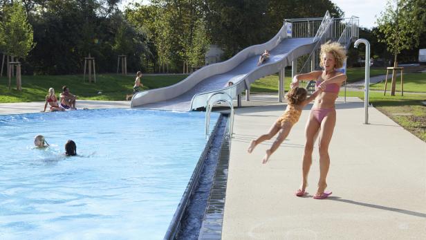Eine Frau wirft ein kleines Mädchen am Beckenrand in die Luft.
