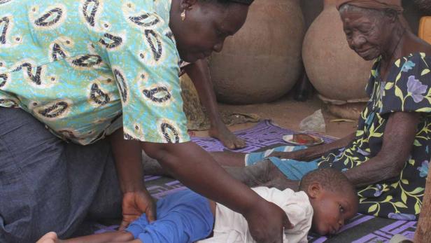 Eine Frau behandelt ein Kind, während eine ältere Frau daneben sitzt.