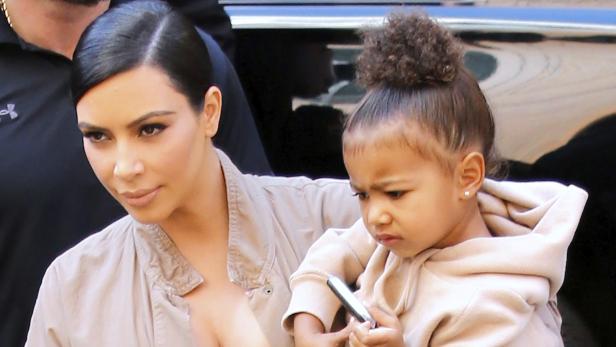 Kim Kardashian mit ihrer Tochter, die ein Handy in der Hand hält.