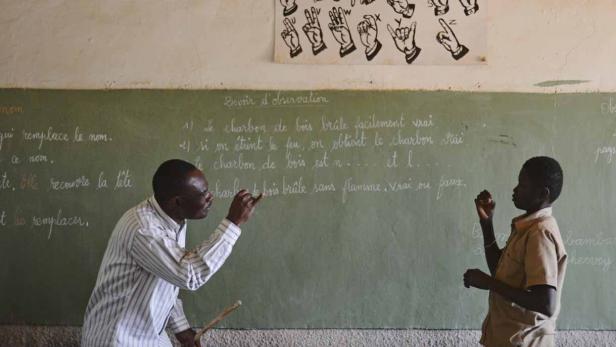 Ein Lehrer erklärt einem Schüler etwas an einer Tafel in einem Klassenzimmer.
