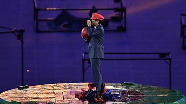 Ein Mann im Mario-Kostüm steht auf einer Bühne und hält einen roten Ball.