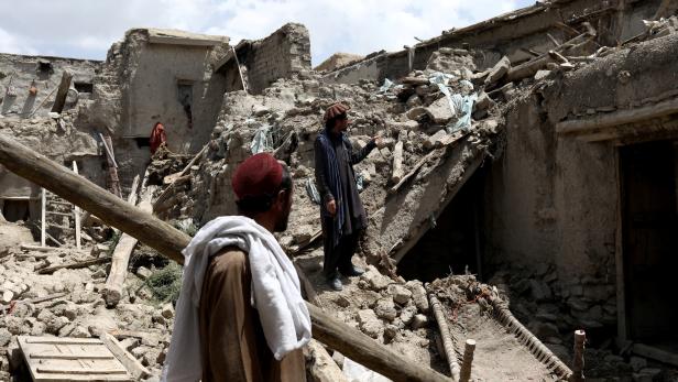 Afghan men stand on the debris of a house that was destroyed by an earthquake in Gayan