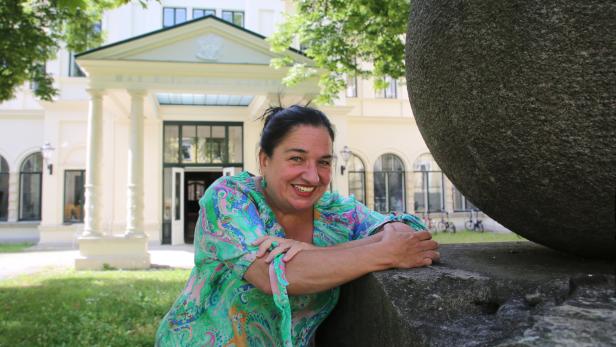 Eine lächelnde Frau lehnt an einer Steinkugel vor dem Max Reinhardt Seminar.