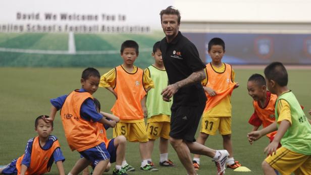 David Beckham trainiert eine Gruppe junger Fußballspieler auf einem grünen Feld.