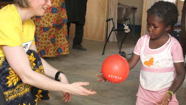 Ein Mädchen kniet und spielt mit einer Frau einen roten Ball zu.