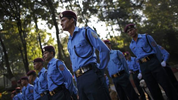 Eine Reihe von Polizisten in blauen Uniformen und roten Baretts steht im Freien.