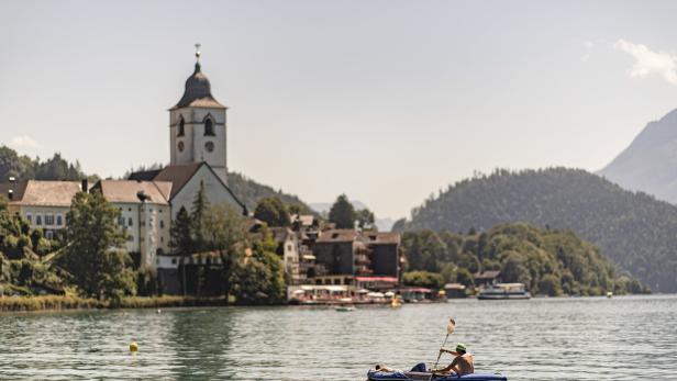 Ein Mann paddelt in einem Schlauchboot auf dem Wolfgangsee, im Hintergrund St. Wolfgang.