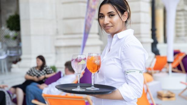 Eine Kellnerin serviert zwei erfrischende Getränke auf einer Terrasse.