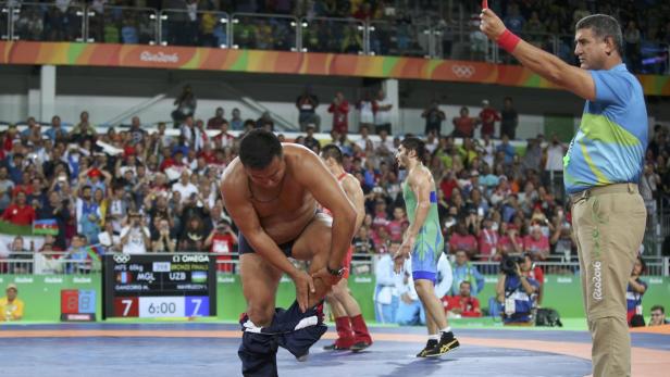 Ein Ringer zieht sich während eines Kampfes die Hose aus, während ein Schiedsrichter zusieht.