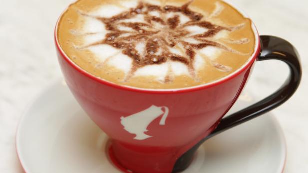 Ein Cappuccino mit einem dekorativen Mosaikmuster in einer roten Tasse.