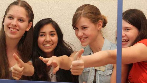 Vier lächelnde junge Frauen posieren hinter einem blauen Rahmen.