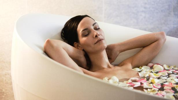 Eine Frau entspannt in einer Badewanne voller Rosenblätter.