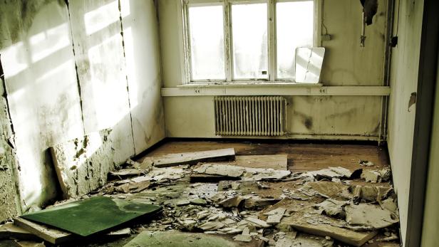 Ein verwüsteter Raum mit Bauschutt und einem Fenster mit Heizkörper.